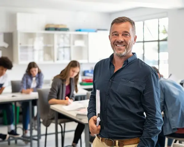 Professore sorridente in aula con studenti. La sua laurea per insegnare alle superiori è evidente dalla sua sicurezza.