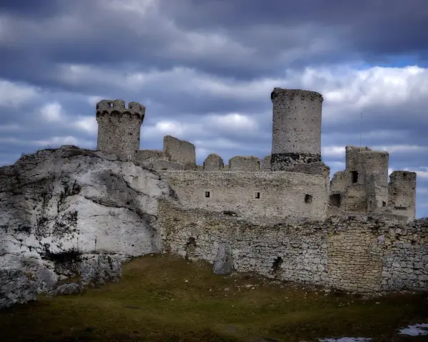 Ruiny zamku Ogrodzieniec na skale, z wieżami i murami, pod burzowym niebem. Idealne miejsce na trasę pełną historii.