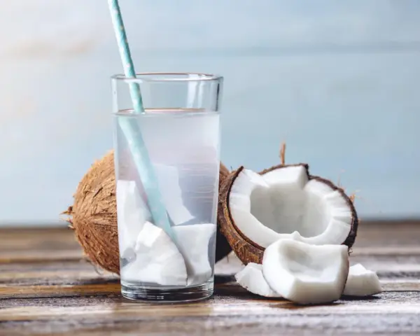 Verre d'eau de coco fraîche avec des morceaux de noix de coco. Une boisson naturelle pour soulager la constipation.