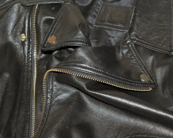 Dettaglio di una giacca in ecopelle nera con zip dorata e bottoni a pressione. Si pensa a come lavare giacca ecopelle in lavatrice.