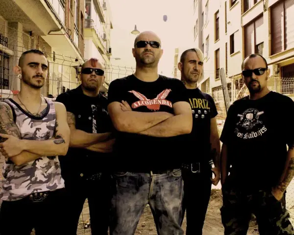 Cinco hombres con estética punk posan en una calle, listos para el rebel fest.