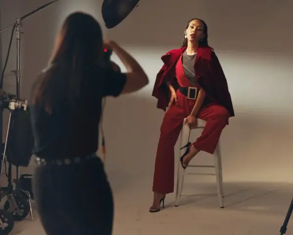 Sesja zdjęciowa w studio. Modelka w czerwonym stroju pozuje na stołku. Fotografka robi zdjęcie. Zastanawiasz się, ile zarabia fotograf?