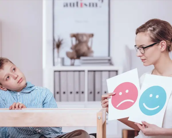 Bambino con autismo durante un test, mentre un terapista mostra faccine felici e tristi.