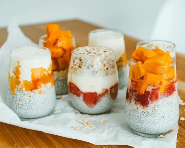 Pyszny deser chia z mango i truskawkami w szklankach, ułożony warstwowo z jogurtem i płatkami owsianymi.