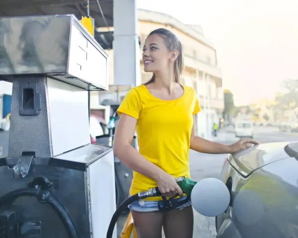 Uśmiechnięta kobieta tankuje auto. Zastanawia się, jak przelać punkty Vitay z karty na kartę, by zaoszczędzić na paliwie.