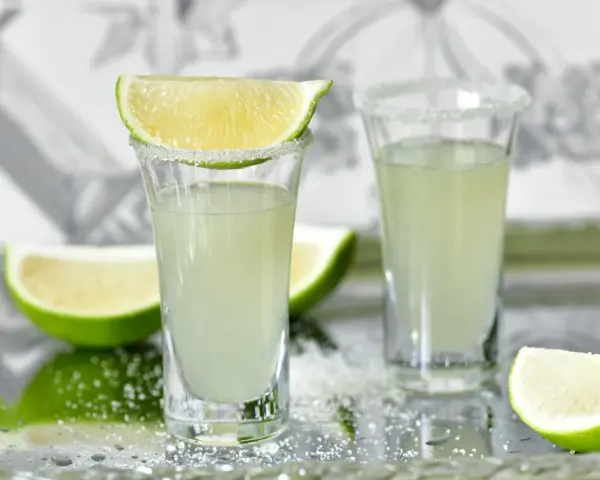 Dwa kieliszki z drinkiem Kamikadze, ozdobione solą i plasterkami limonki. Idealny przepis na orzeźwiający shot.