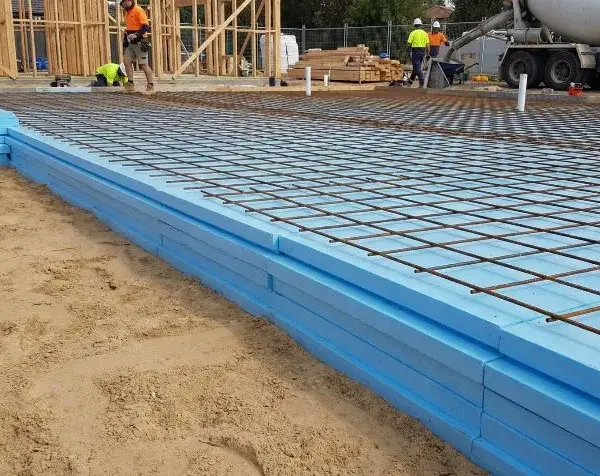 Układanie płyt XPS na fundamentach pod wylewkę betonową. Widoczna siatka zbrojeniowa.