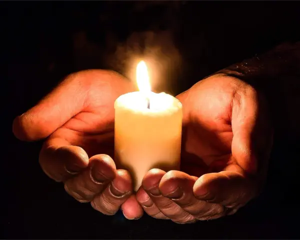 Hände umschließen eine Kerze, die ein warmes Licht spendet. Ein Symbol für evangelische Gebete und Hoffnung in der Dunkelheit.