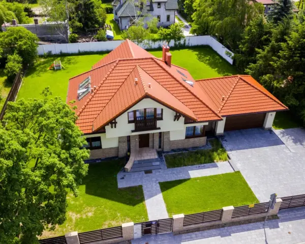 Piękny dom 200m2 z pomarańczowym dachem, otoczony zielonym ogrodem i drzewami. Podjazd z kostki brukowej prowadzi do garażu.