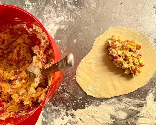 Fyllning till piroger recept läggs på deg. En röd skål med fyllning syns till vänster.