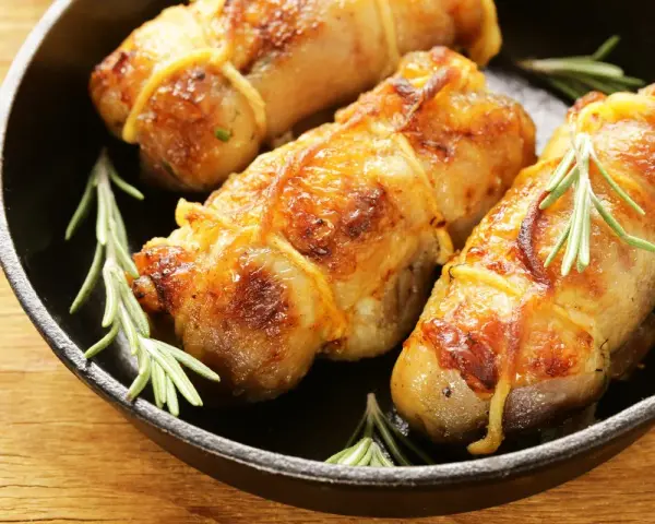 Involtini di pollo dorati e succulenti, legati con spago da cucina e guarniti con rametti di rosmarino, in una padella di ghisa.