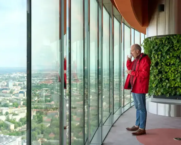 Mężczyzna pije kawę, podziwiając panoramę Wrocławia z tarasu widokowego. Sprawdź Sky Tower Wrocław cennik, by poznać ceny biletów.