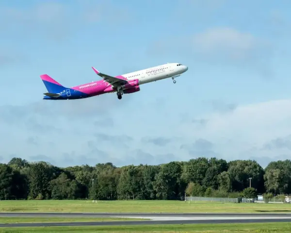 Samolot Wizz Air wznosi się na tle błękitnego nieba z chmurami.