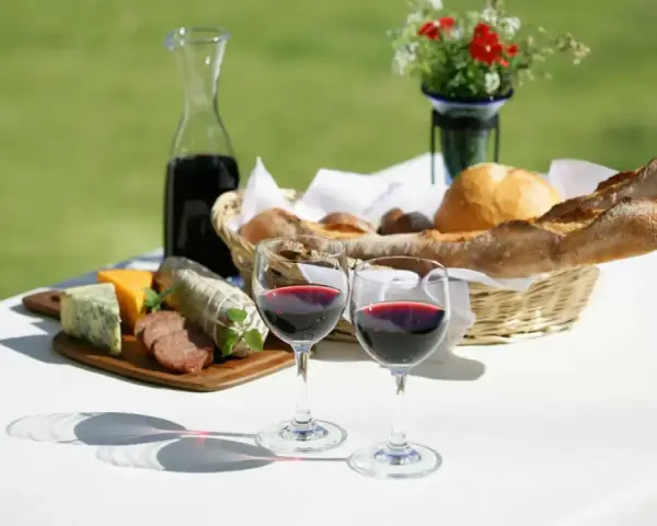Dwa kieliszki pełne rubinowego pinot noir wina, obok deska serów, wędlin i kosz świeżego pieczywa.