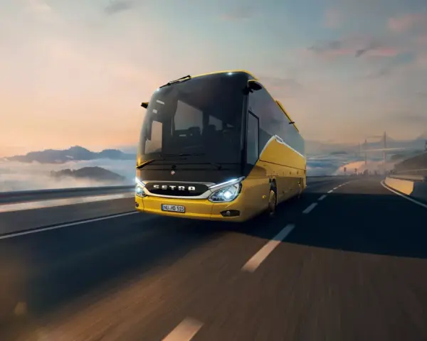 Żółty setra autobus pędzi po autostradzie wśród chmur i gór, w stronę mostu.
