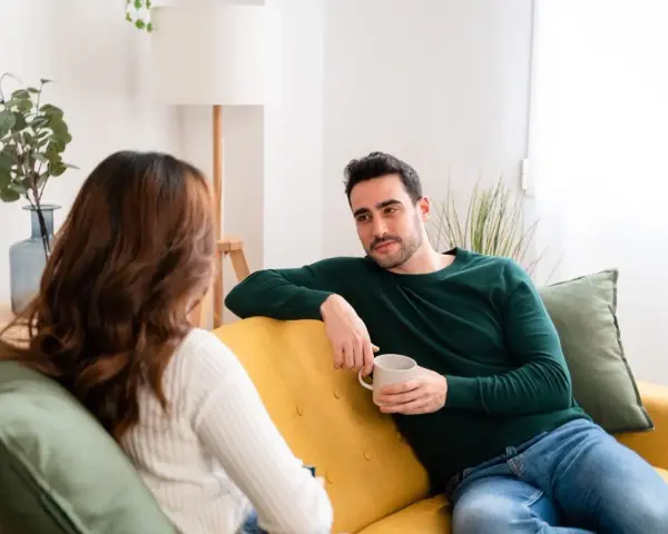 Coppia sul divano, lui con tazza in mano, lei di spalle. Una conversazione tesa, forse legata a **ADHD e tradimento**.