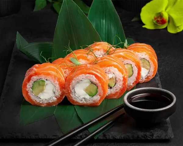 Roladki sushi z łososiem i awokado, podane na liściach. Inspiracja, jak zrobić sushi.