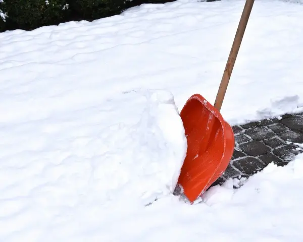 Pomarańczowa łopata do śniegu wbita w zaspę na ośnieżonym chodniku.