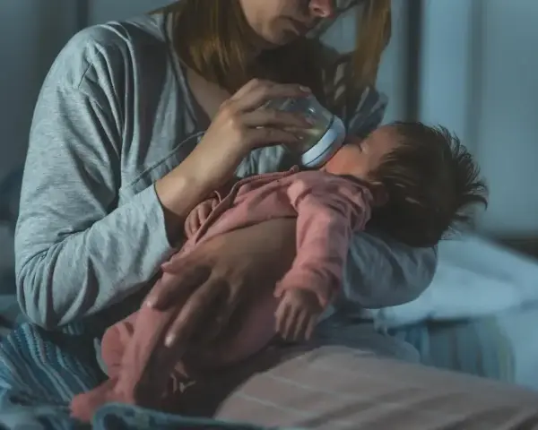 Mama karmi butelką niemowlę, które obudziło się w nocy z płaczem.