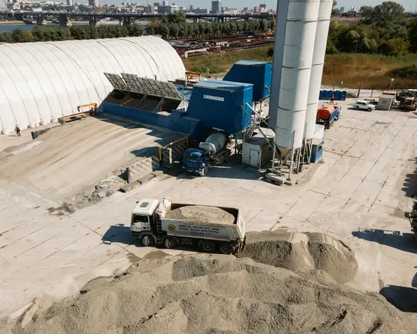 Beton skład z ciężarówką wyładowującą materiał. W tle silosy i budynki przemysłowe.