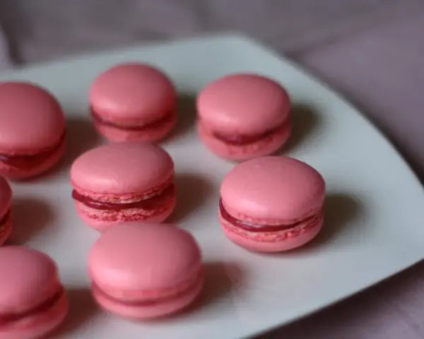 Rosa macarons med hallonfyllning på en vit tallrik. Perfekt för ett macarons recept.