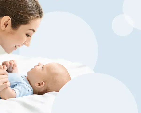 Uśmiechnięta mama pochyla się nad dzieckiem, które świadomie mówi "mama".