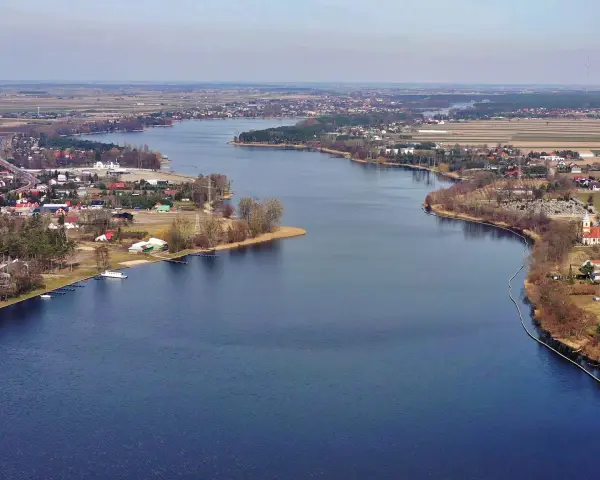 Rozległe jezioro Mikorzyńskie otoczone zabudowaniami i polami. W oddali widać kościół i cmentarz.