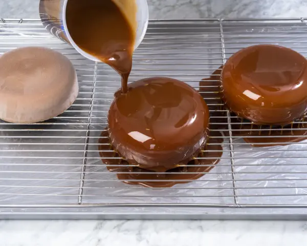 Dolce lucido ricoperto da una colata di cioccolato. La glassa scende sui lati, creando un effetto invitante.