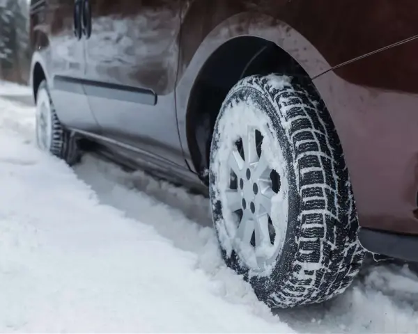 Un'auto marrone avanza su una strada innevata, le ruote dotate di pneumatici chiodati per affrontare il ghiaccio e la neve.