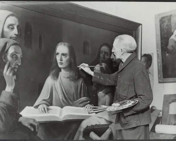 Giuliano Ruffini, artiste peintre, retouche une toile représentant des figures religieuses. Il tient pinceaux et palette.