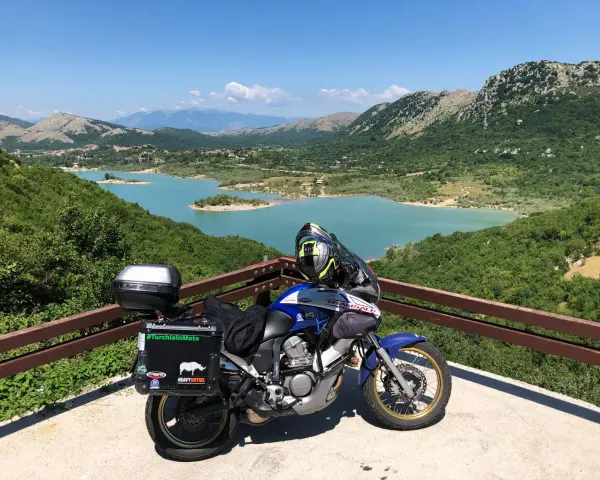 Moto pronta per avventurosi giri in moto nel Lazio, con un panorama mozzafiato sul lago turchese e le montagne verdi.