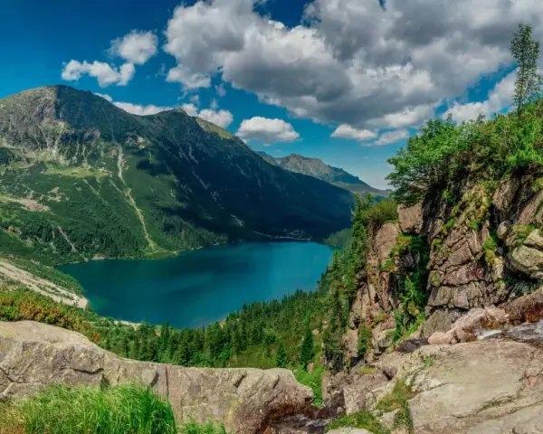Majestatyczne tatry szczyty otaczają turkusowe Morskie Oko. Chmury na niebie dodają dramatyzmu krajobrazowi.