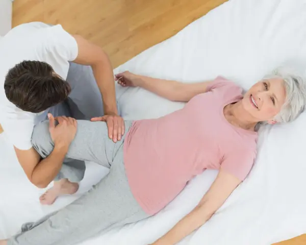 Physiotherapeut unterstützt ältere Frau bei Übungen für den Beckenboden. Sie lächelt zufrieden.