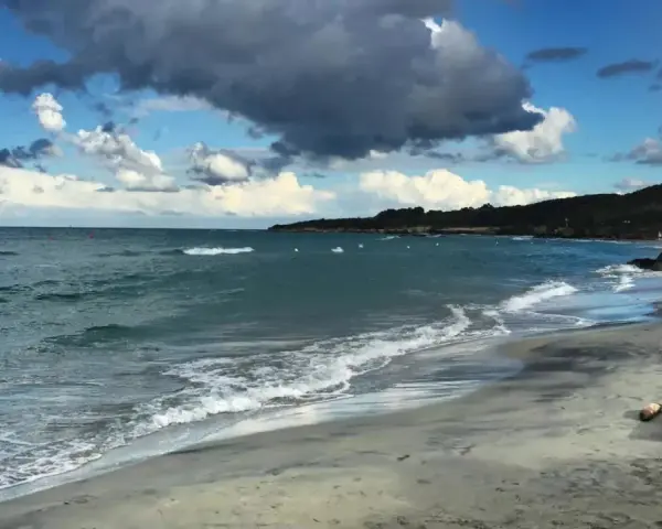Onda che lambisce la spiaggia sabbiosa dell'Isola d'Elba, con il mare azzurro e nuvole scure nel cielo.
