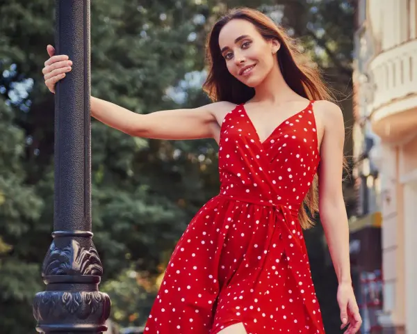 Junge Frau in einem roten Kleid mit Polka Dot Muster lehnt an einer Laterne.
