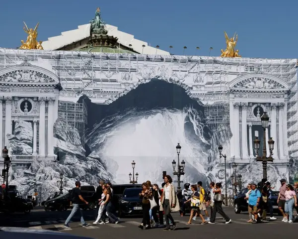 Des passants traversent devant l'Opéra Garnier, dont la façade est recouverte d'une bâche monumentale simulant des travaux et une arche rocheuse.