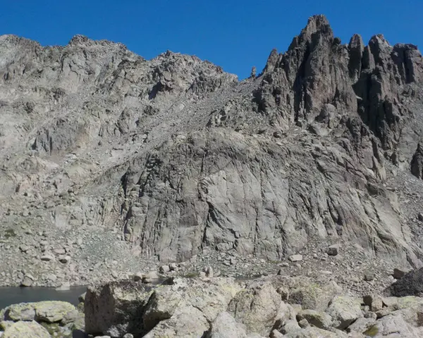 Vetta frastagliata di un monte rotondo, con rocce grigie e un lago alpino sullo sfondo.