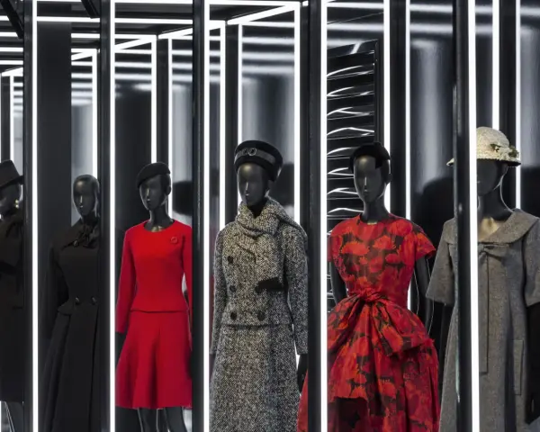 Manichini con abiti eleganti, un omaggio all'eleganza e all'origine Dior. Rossi, neri e grigi, con cappelli e sciarpe.