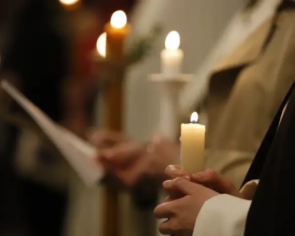 Dłonie trzymają płonące świece, symbolizujące poświęcenie ognia podczas uroczystości.