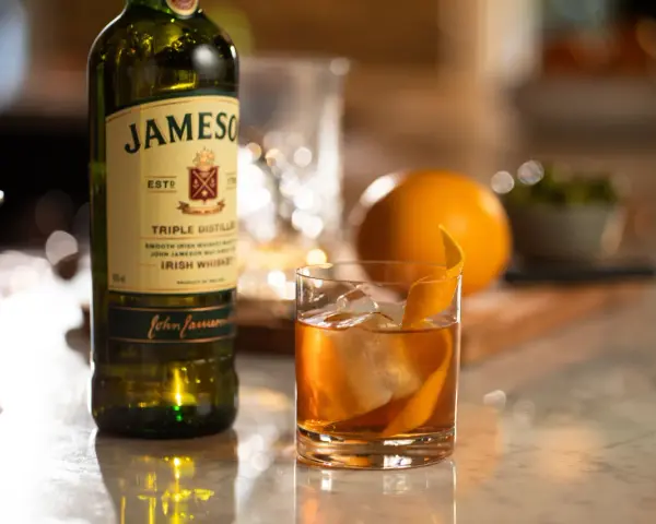 Old Fashioned na bourbonie czy na żytniej whisky? Jameson Irish Whiskey obok drinka z pomarańczą i lodem.