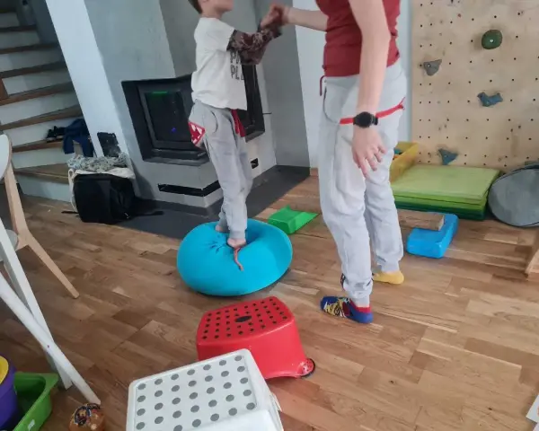 Dziecko ćwiczy równowagę na niebieskiej poduszce, część domowej ścieżki sensorycznej dla dzieci.