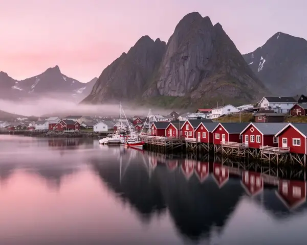 Röda fiskestugor vid vattnet i Lofoten, med berg och rosa himmel. En dröm om norrsken.