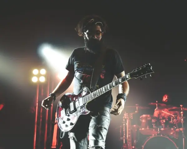 Un guitariste charismatique d'un groupe de rock mythique, en pleine performance sur scène, éclairé par des projecteurs.