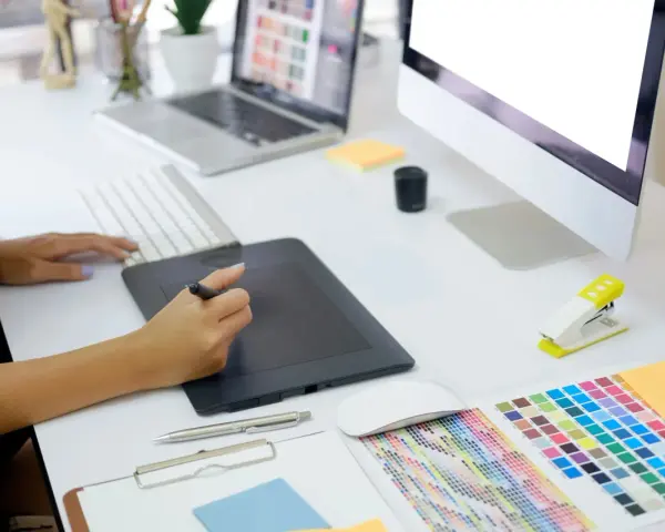 En grafisk designer arbetar vid sitt skrivbord med en ritplatta, tangentbord och en färgkarta. En bra **concept vista prisjakt** för kreativa projekt.