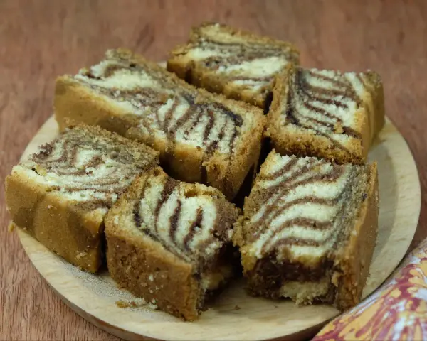 Kawałki ciasta zebra, z charakterystycznym wzorem przypominającym paski zebry, ułożone na drewnianej desce. To smak dzieciństwa, jak ze starego przepisu na ciasto zebra.