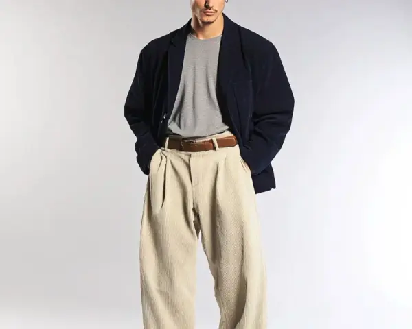 Uomo con spezzato giacca blu scuro, maglietta grigia e pantaloni beige a vita alta.