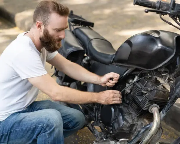 Uomo con barba lavora sul motore di una moto. Controlla i cavi, forse per il tempo di ricarica batteria moto 12v.