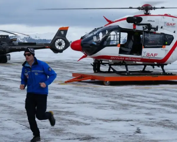 Ratownik w niebieskiej kurtce biegnie na tle dwóch helikopterów w Austrii, gotowych do akcji po lawinie.