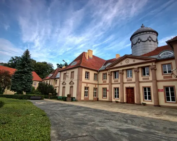 Pałac Maltzanów z charakterystyczną wieżą i czerwonym dachem, otoczony zielenią.