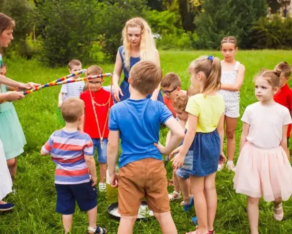 Des animateurs et des enfants jouent dehors dans l'herbe avec des cerceaux colorés.